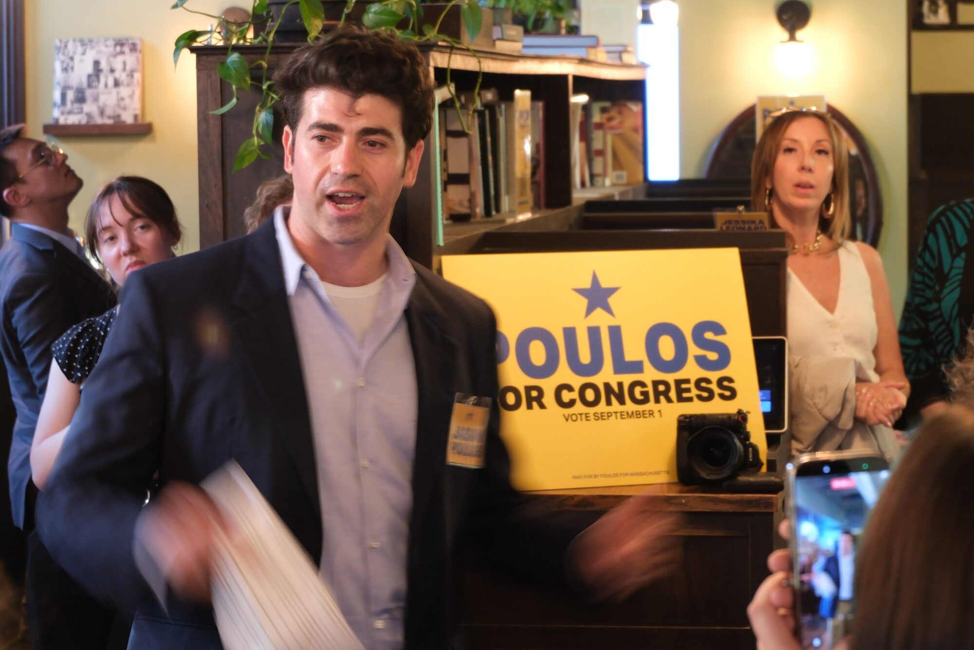 Jason Poulos speaking to supporters beside a Poulos for Congress sign at the Newton fundraiser, Thistle & Leek, June 29, 2026