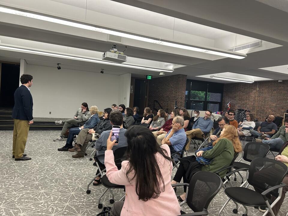 Jason Poulos addressing a seated audience at a town hall in MA-04